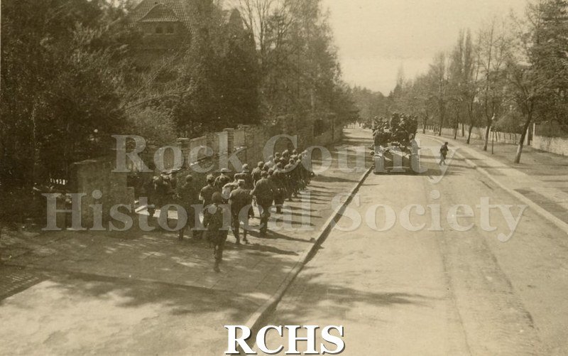 Black and white photograph of soldiers walking on a sidewalk. Back of photo reads: "9).