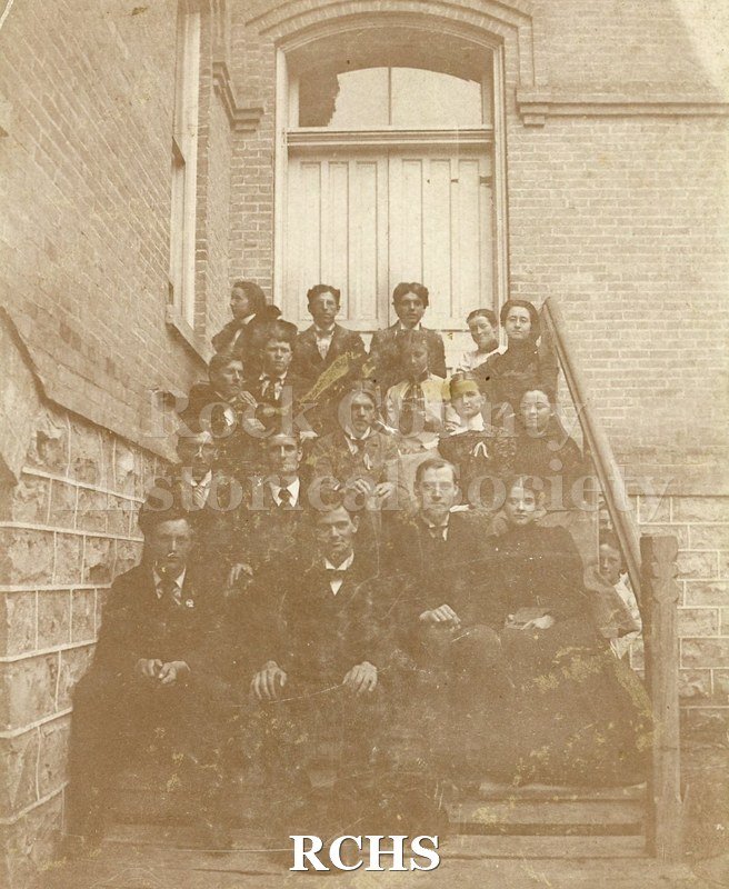 Black and white photograph of Evansville Seminary Family . Several people are sitting on the steps of a building.