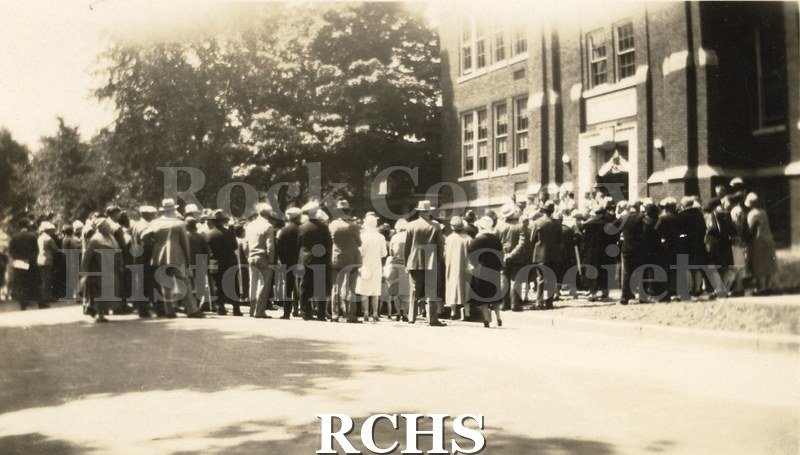 Black and white photograph of a crowd of people gathered outside the entrance of a building, possibly Janesville High School after it was constructed.