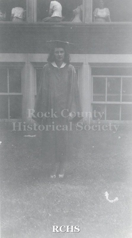 Black and white photograph of Jean McLaughlin in her cap and gown outside Janesville High School.