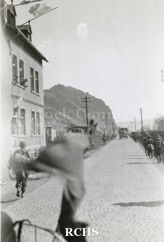 Black and white photograph of a convoy of US soldiers driving down a cobblestone street.