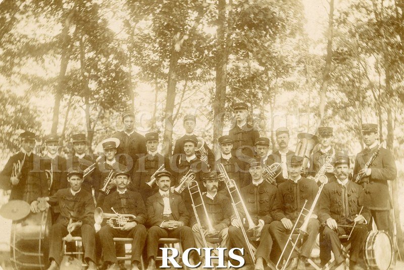Black and white photograph of the Y.M.C.A. Concert Band, Janesville, WI. Shows several men and their instruments. Venue is outdoors.