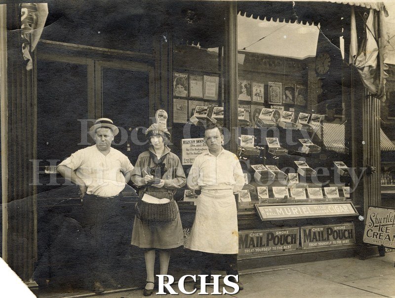 Black and white photograph of Hackett's Cigar Store. Three people are standing in front of a storefront.