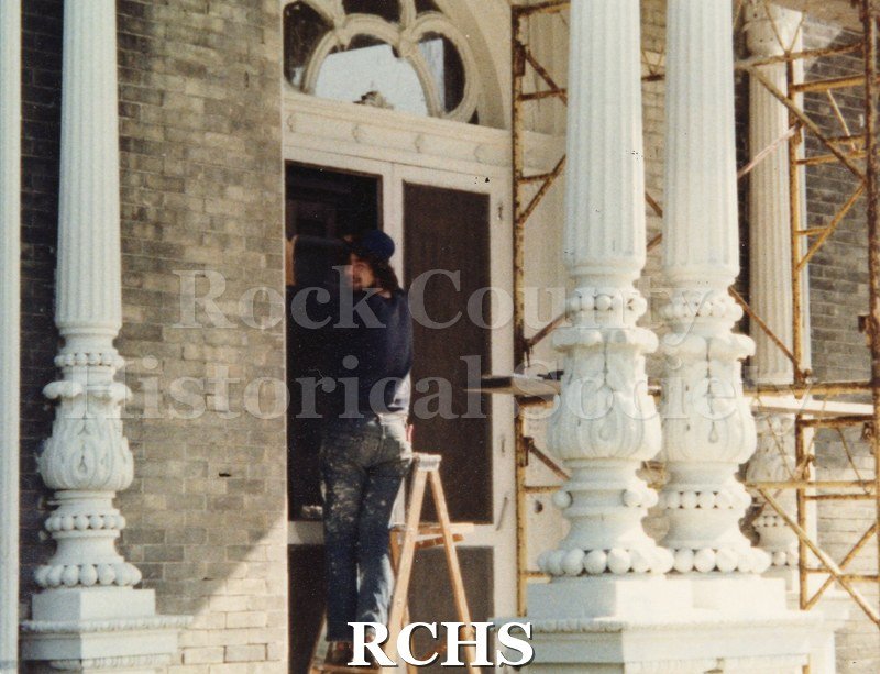 Color photo of the Tallman House front entrance with a workman on a ladder working near the door.