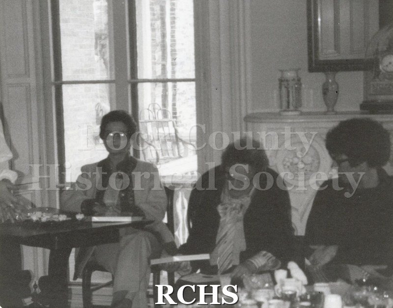 Black and white photograph of three women seated at a table in front of the fireplace in the Tallman House.
