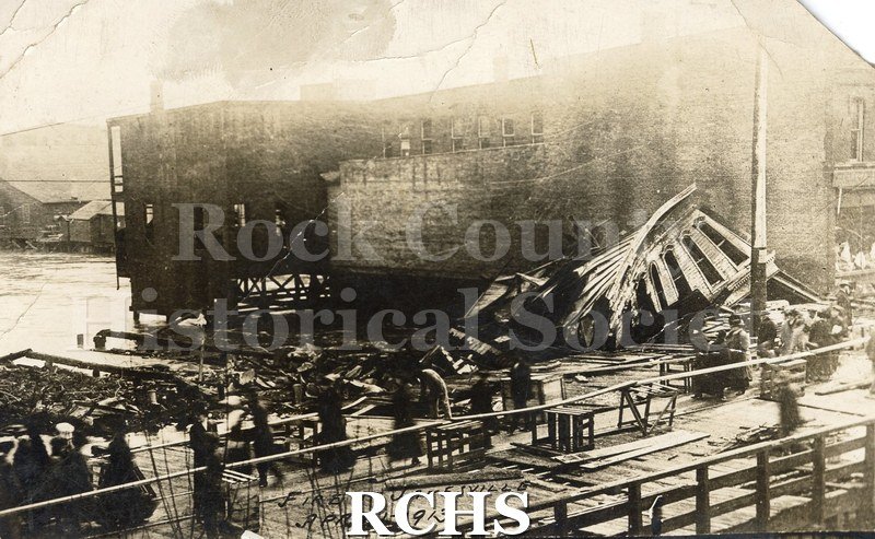 Postcard. Black and white glossy photograph of Milwaukee St. Bridge Fire 4/1/1913. Foreground shows wood railing and bridge with standing people.