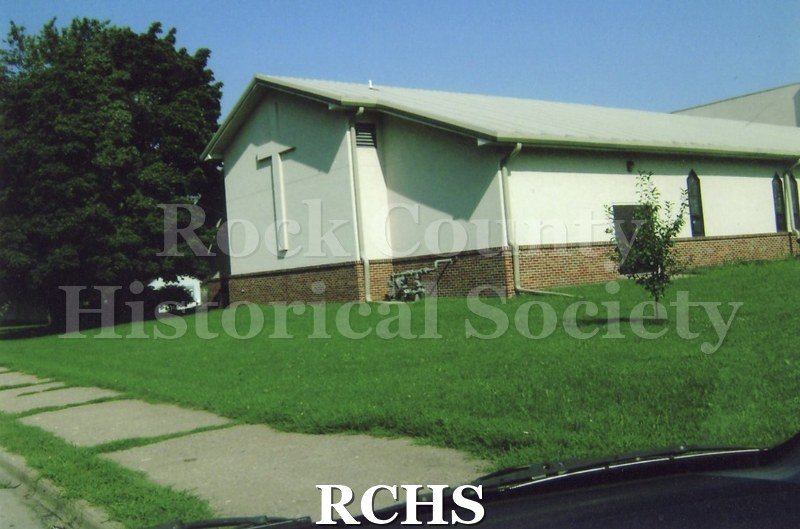Colored photograph of New Life Ministry Pentecostal church, 1400 Harvey St., Beloit. White church with brick down by the foundation.