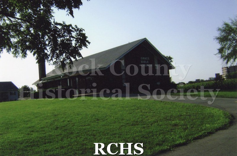 Colored photograph of Grace Bible Church, Baptist, 1928 Colony Ct., Beloit. Dark brick building next to a corn field.