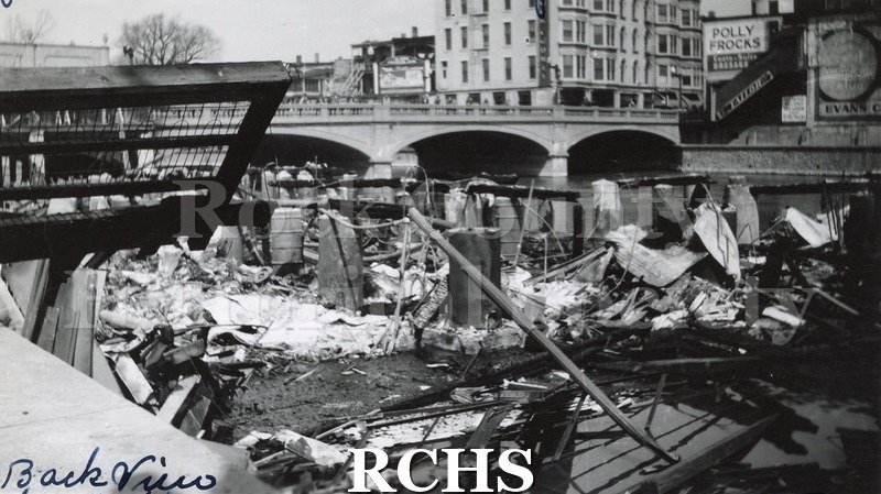 Black and white photograph of Janesville Fire 1942 showing collapsed building back view. Bridge supports, arch and buildings in background.