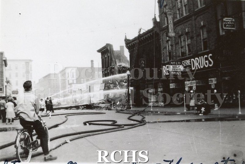 Black and white photograph of Janesville Fire 1942 showing collapsed building, fire hoses in street and one stream of water from fire hose.