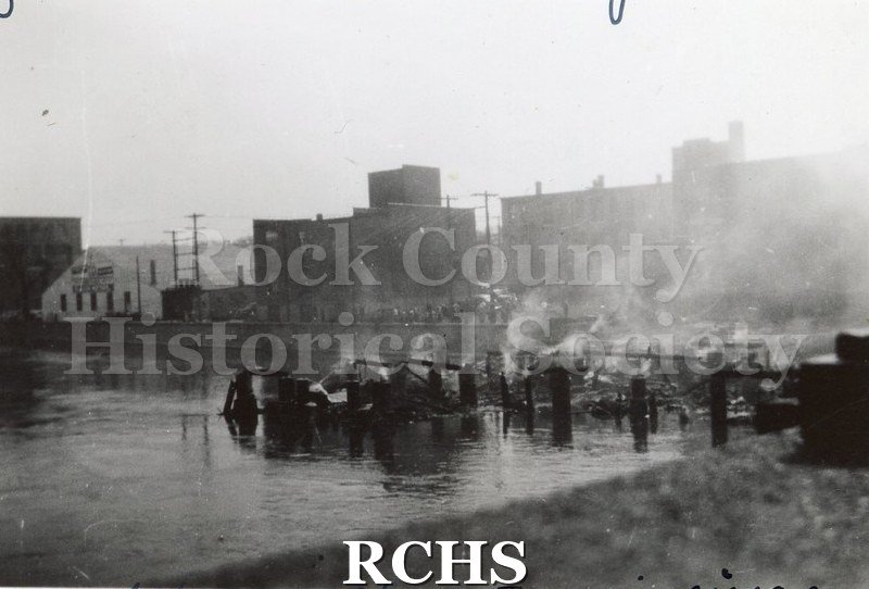 Black and white photograph of Milwaukee Street Bridge Fire 1942 showing smoke, river pilings and buildings in background.
