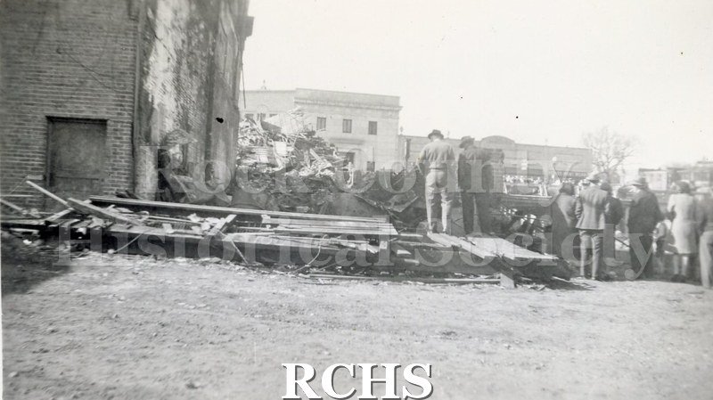 Black and white photograph of Kennedy Drug Store, Milwaukee Street Bridge Fire. Brick building on left, other buildings in background.