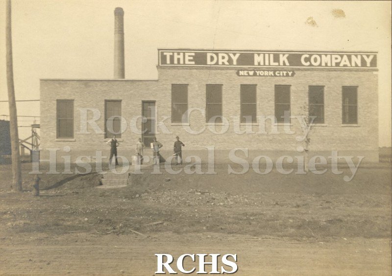 Black and white photograph of four men. Bowman Dairy, Clinton. Four men are standing in front of the Dry Milk Company building.