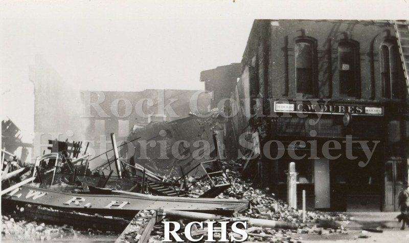 Black and white photograph of the Milwaukee Street Fire 4/13/42. It shows the charred remains of a building next to C. W. Dubes building that is standing.