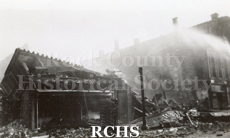 Blackand white photograph of the Milwaukee Street Fire 4/13/42. It shows the charred remains of a building with water being poured n it.