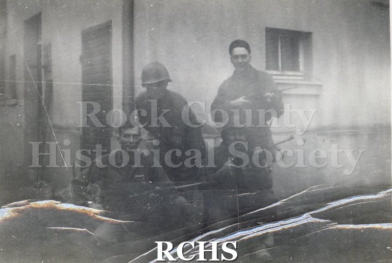 Black and white photograph of Gaddy Adams, Bill Carr and two other unidentified soldiers posed with their guns in an unknown village.