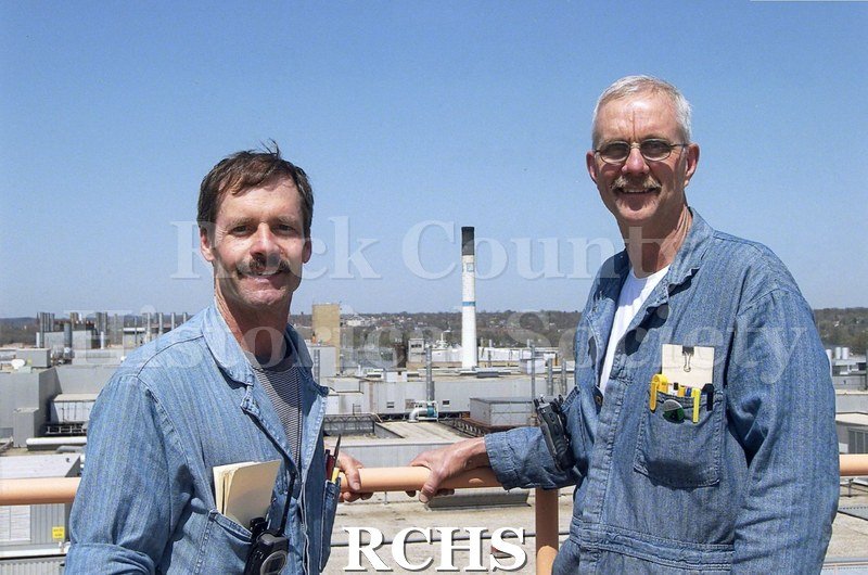 Color photo of Ike Johnson and Curt Wam repairing the rooftop air conditioning unit at the Janesville GM plant.