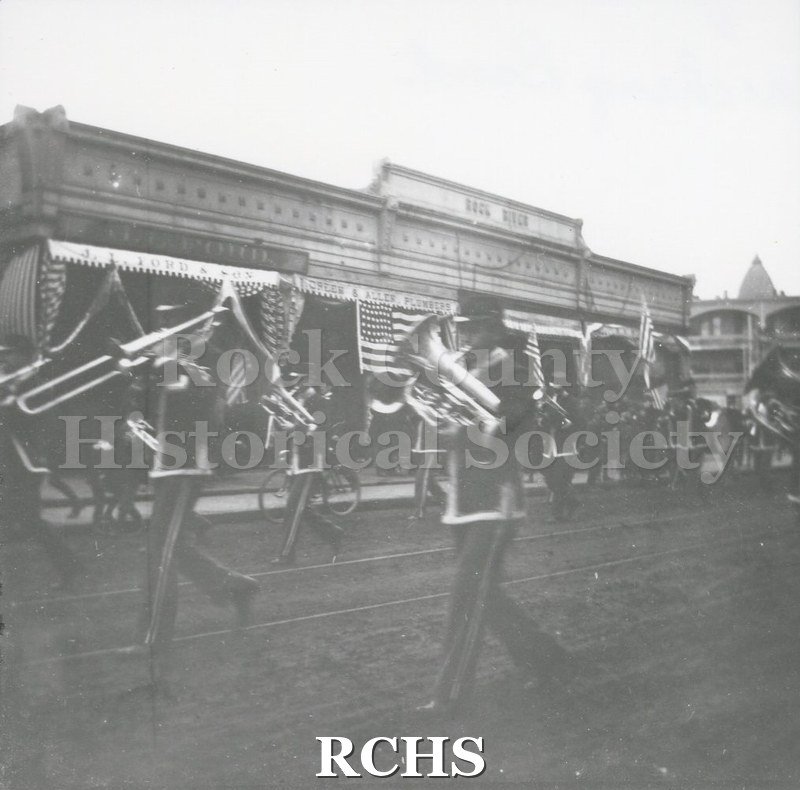 Black and white photograph of a marching band in a parade in downtown Janesville.