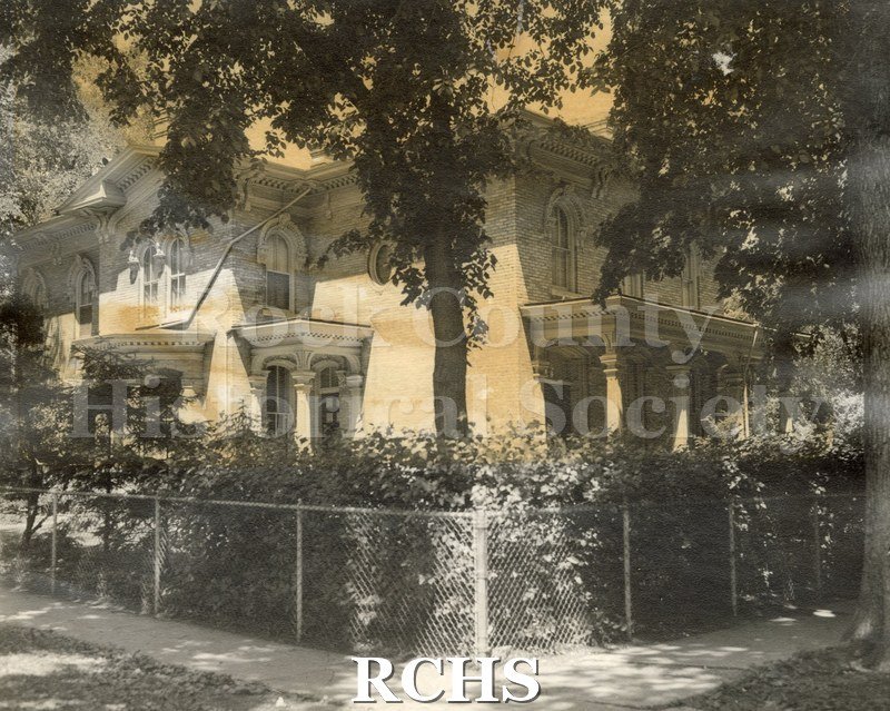 Colored photograph of 220 S. Academy Street, a two story brick house with a pillared porch and a fence around it.