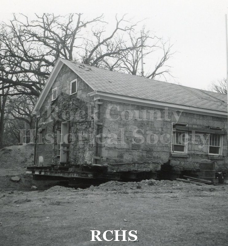 Black and white photograph of the Stone House which has been moved to the campus of the Tallman property. Shows building without the porch and pillars.