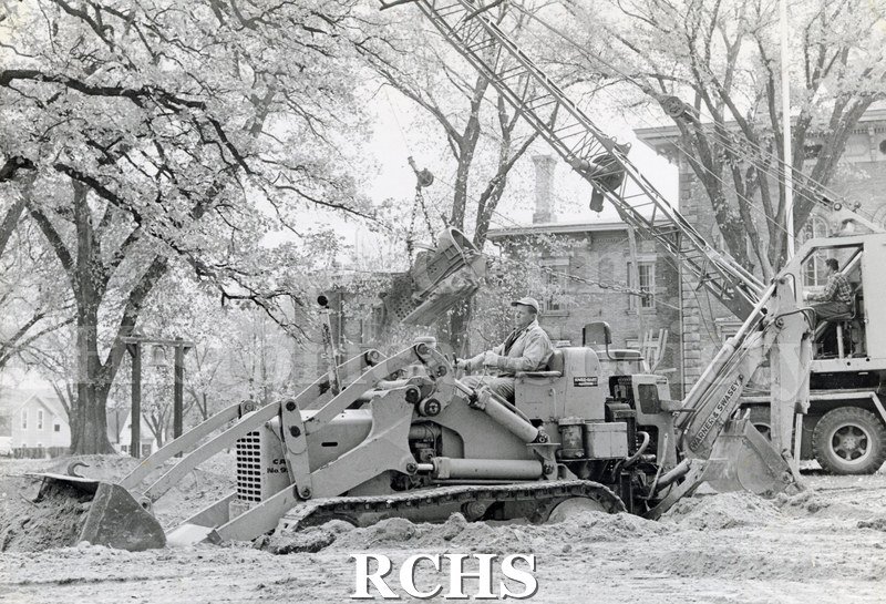 Black and white photograph of an excavator being operated near the Tallman House, digging a foundation for the Stone House.