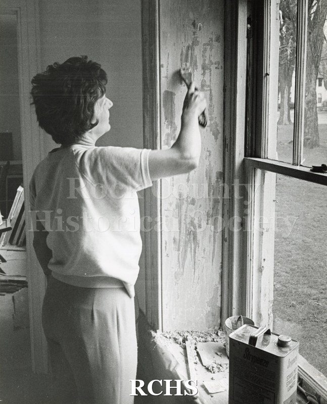 Black and white photograph of Mrs. James Stauff scraping paint at the RCHS Stone House.