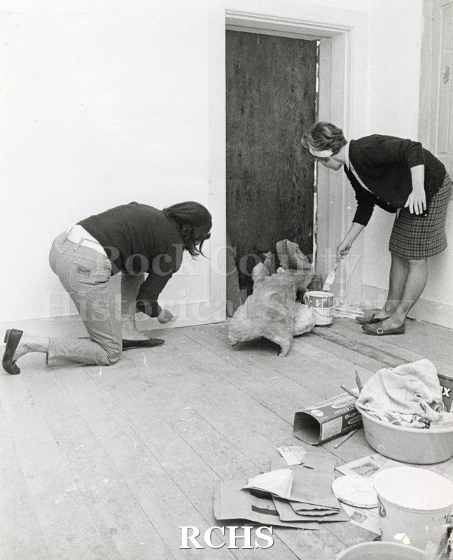 Black and white photograph of Mrs. Roy Meyers and Mrs. Richard Rost painting the RCHS Stone House.