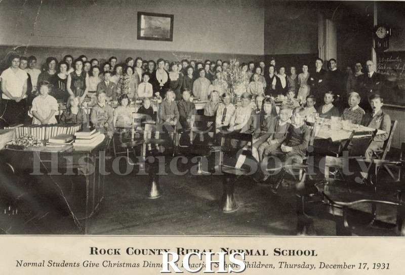 Black and white photograph of Rock County Rural Normal School. The students and teachers are in a classroom with a table set for Christmas dinner Thursday, December.