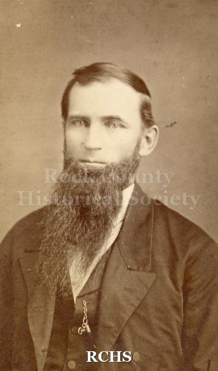 Black and white photograph of Matthew Van Allen. Above waist, man with dark hair, deep part on his left. Full beard.