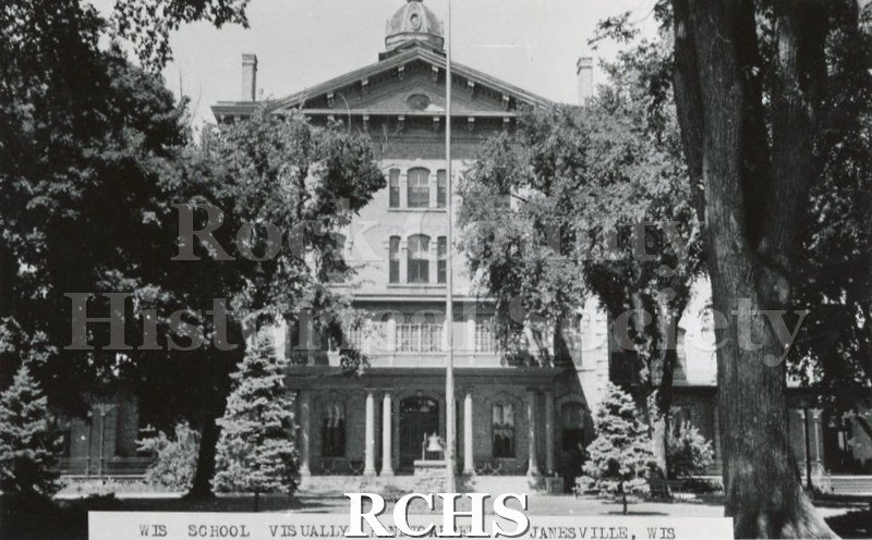 Black and white photograph of Wisconsin School for the Visually Handicapped. Shows a building with flag pole, bell and many trees in front.