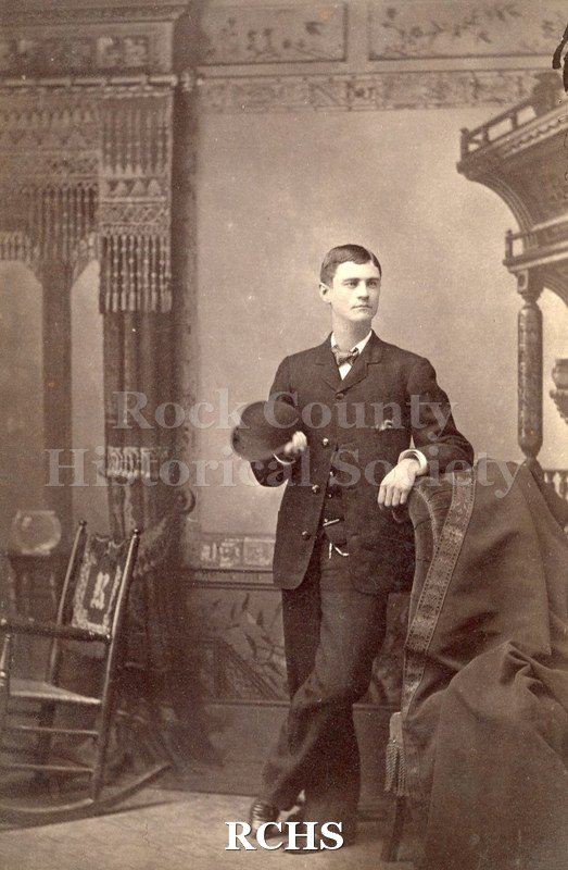 Black and white photograph of H. S. McGiffen standing and leaning on chair back.