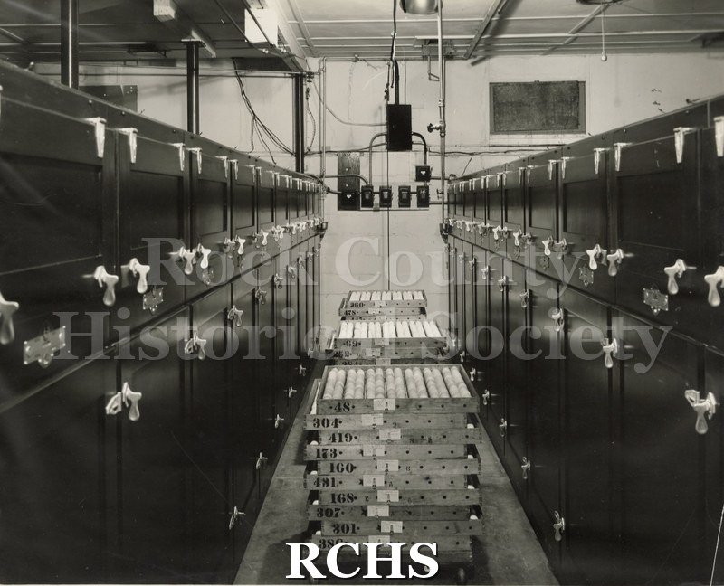 Black and white photograph of Blackhawk Hatchery interor. Shows two rows of dark cabinets with latches, possibly incubators, on each side.