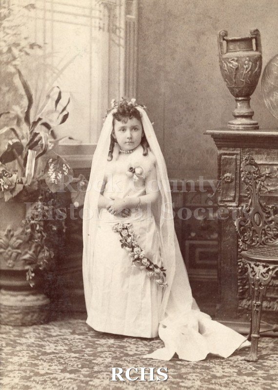 Black and white photograph of Hazel Underhill 1896 wearing a white communion dress and communion veil, posing for a photograph in a studio.