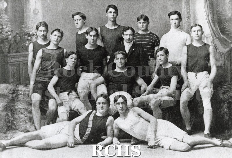 Black and white photograph of the Janesville High School Track Team. There are 11 unidentified men sitting and standing and two are laying down in the front.