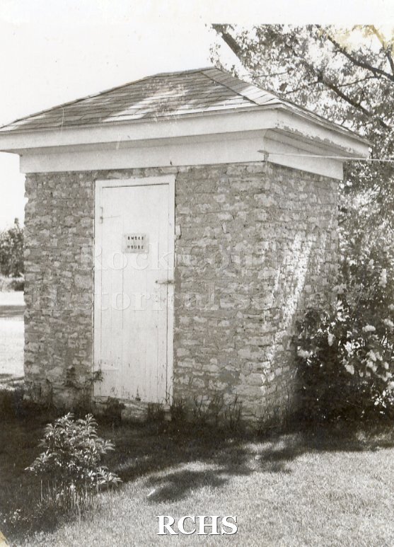 Black and white photograph of Bartlett House Smoke House, Beloit, WI., a small brick building with a sign on the door: "Smoke House".