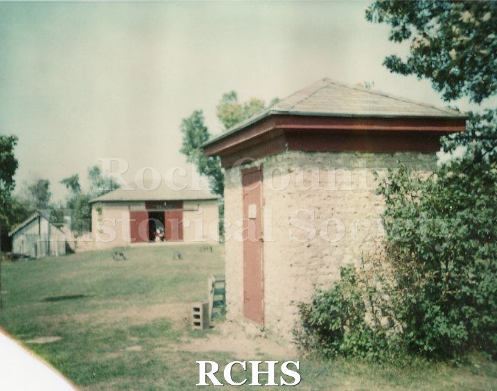 Color photo of the smoke house and barn on the Bartlett Museum grounds.