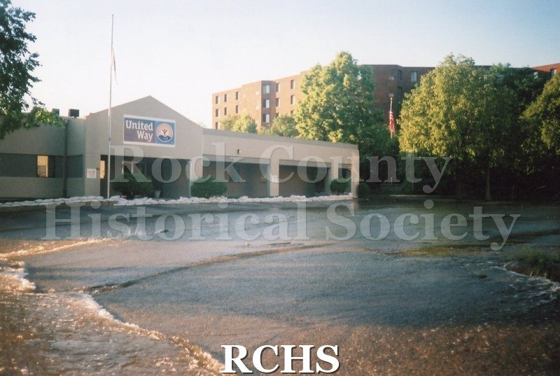 Color photo of the United Way parking lot during the 2008 flood in Janesville. Garden Court Apartments are visible behind the United Way building.