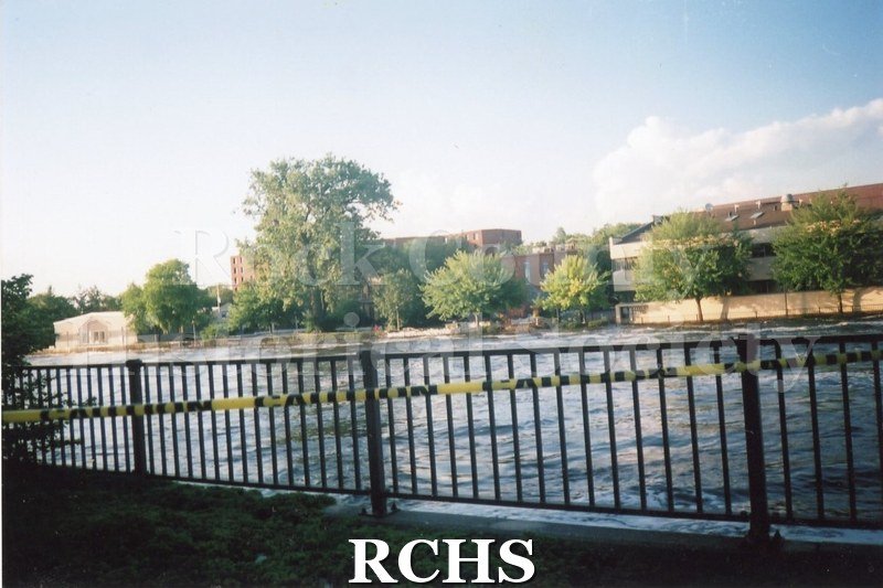 Color photo of the Rock River during the 2008 flood in Janesville. Railing and caution tape in front of photo.