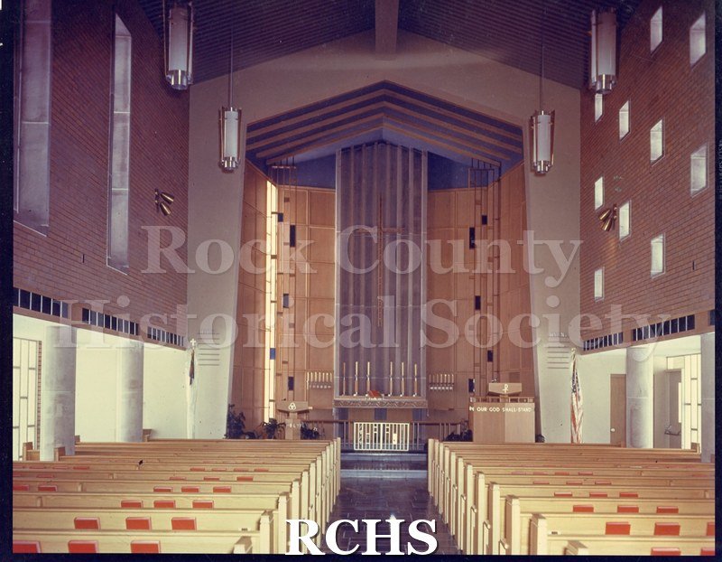IPhotograph. Colored photograph of the interior of an unidentified church, showing the pews looking toward the altar.