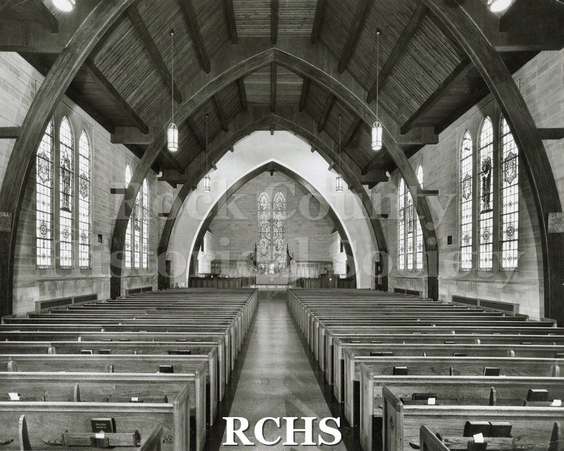 Black and white photograph of the interior of an unidentified church, looking toward the altar from behind the pews.