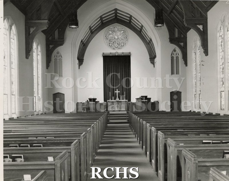 Black and white photograph of the interior of First Methodist Church, Seguin, Texas, looking toward the altar. There is a round stained glass window above the altar.