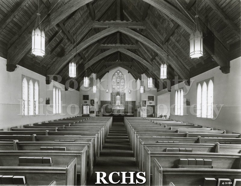 Black and white photograph of the interior of unidentified church in Chicago, IL, looking toward the altar. There is an arched stained glass window above the altar.