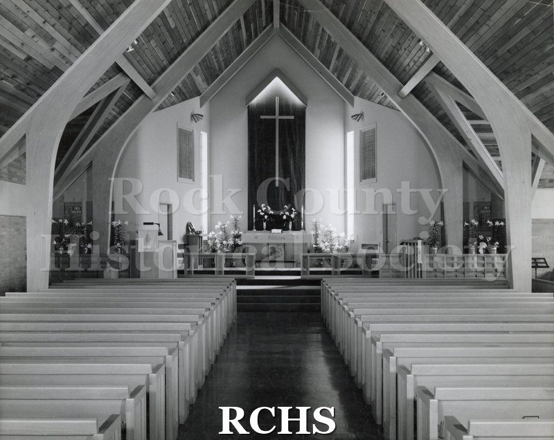 Black and white photograph of the interior of Agustann Lutheran, Fonamondu, N.Y., decorated for Easter. There are several lily plants placed around the church.