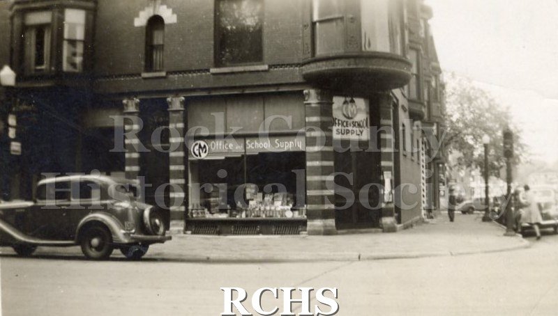 Black and white photograph of the exterior of C&M Office and School Supply store on street corner.