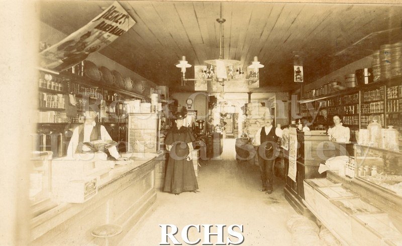 Black and white photograph of the interior of Conrad Bros. Grocery. Gas lamp hanging from ceiling.