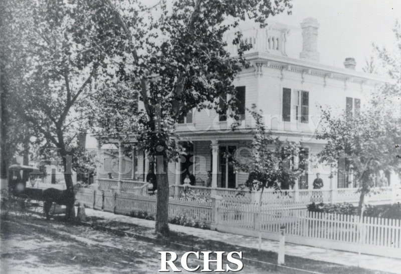 Black and white photograph of 210 S Main St. The image shows a white house with black shutters and cupola. 2 chimneys visible.