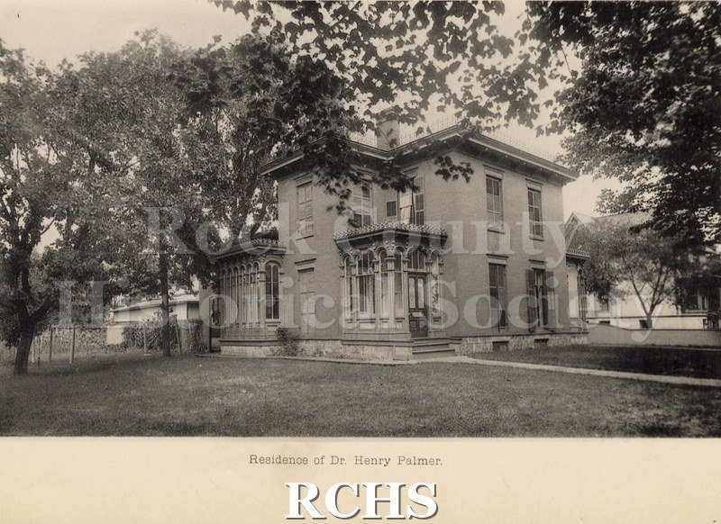 Black and white photograph of the residence of Dr. Henry Palmer. Shows a two story house with two porches, one in front and one on the side.