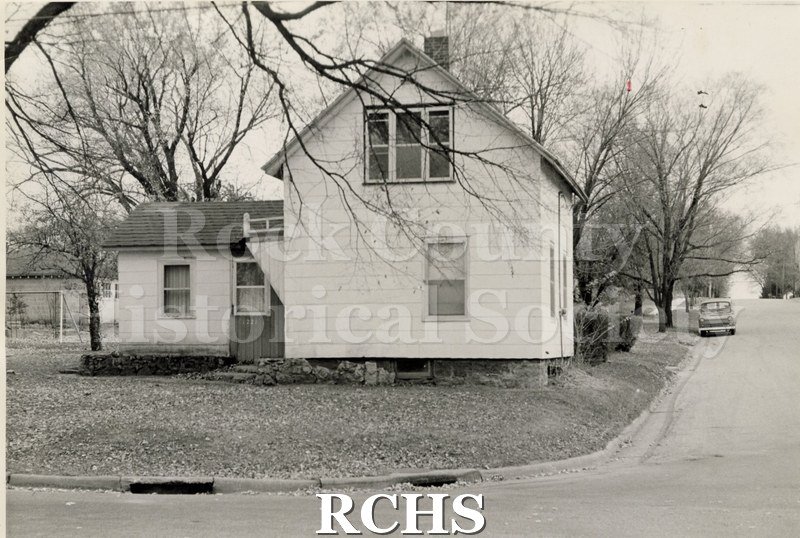 Black and white photograph of a house on S. Pearl Street, Janesville, WI. House has two stories on the right side and a one story entrance on the left.