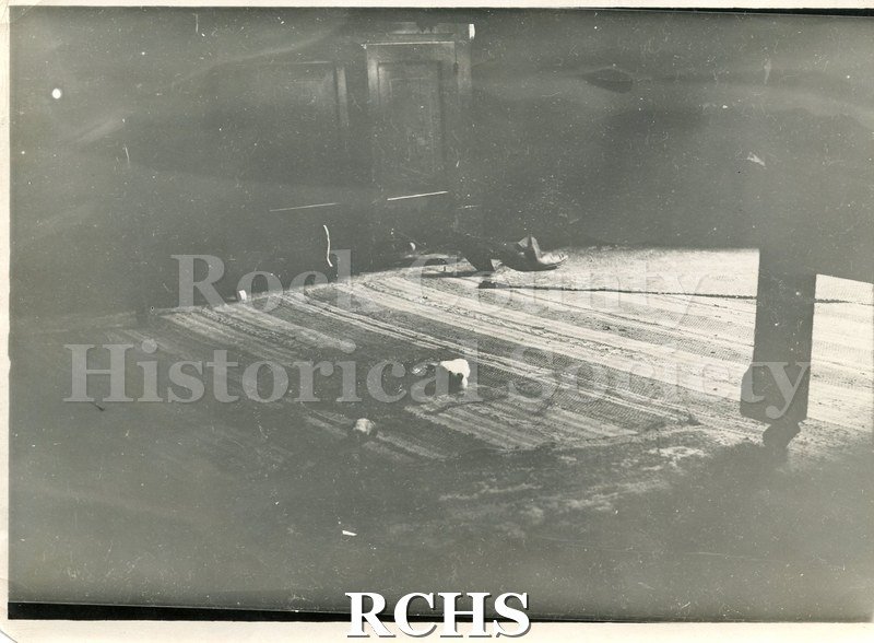Black and white photograph of Locust Street house. Shows the inside of a house. On the rug is a shoe and other unidentifiable items.