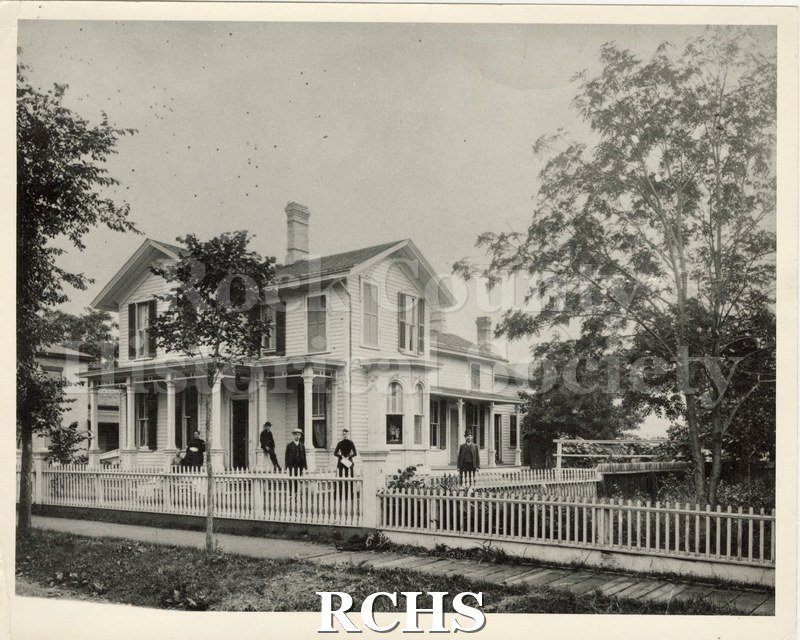 Black and white photograph of the Hemming Family home, 165 Cherry St., Janesville. Shows a two story house with a picket fence around it.